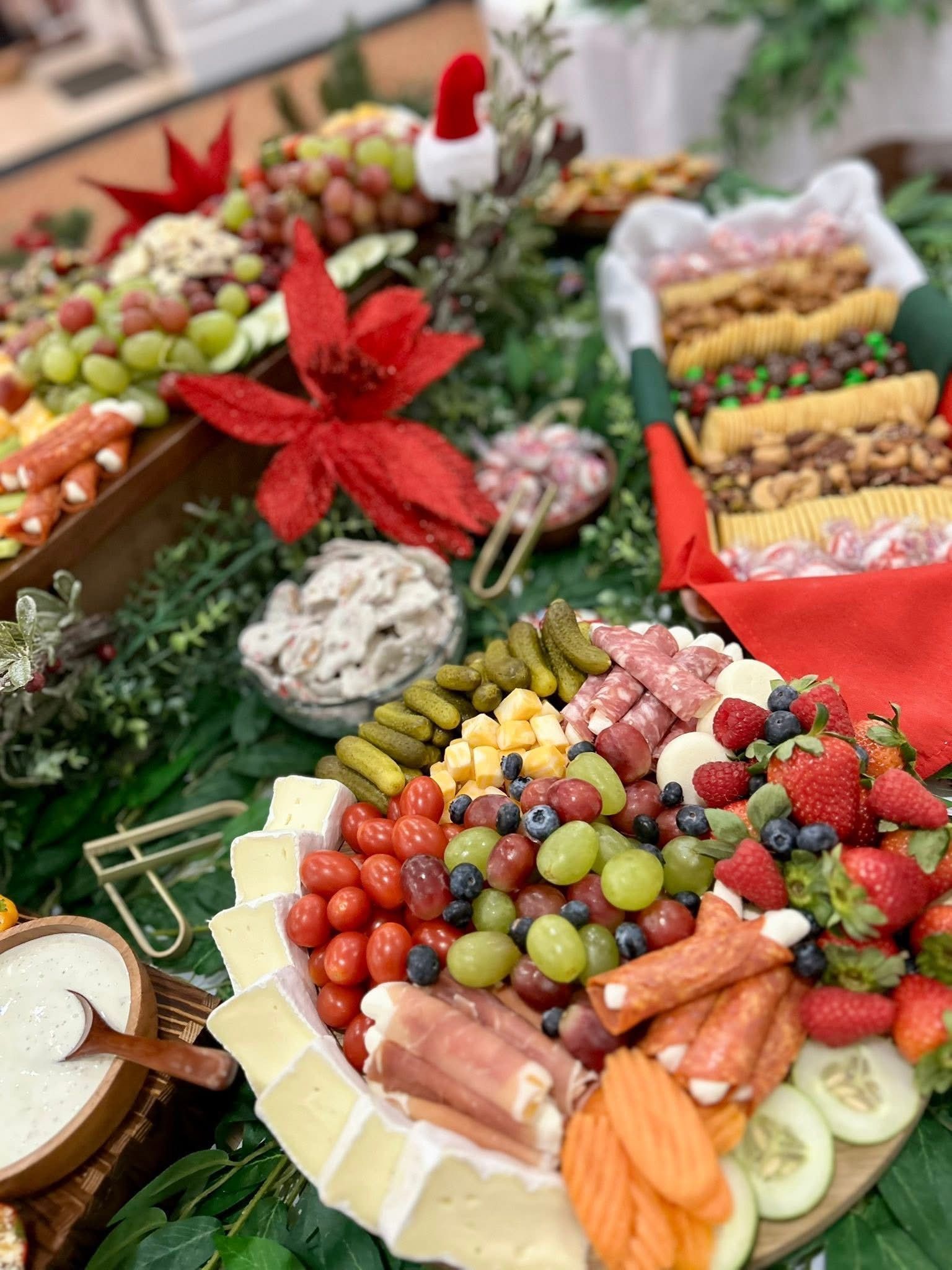 A festive charcuterie board with various snacks, fruit, and dips, arranged on greenery, with a Santa hat.