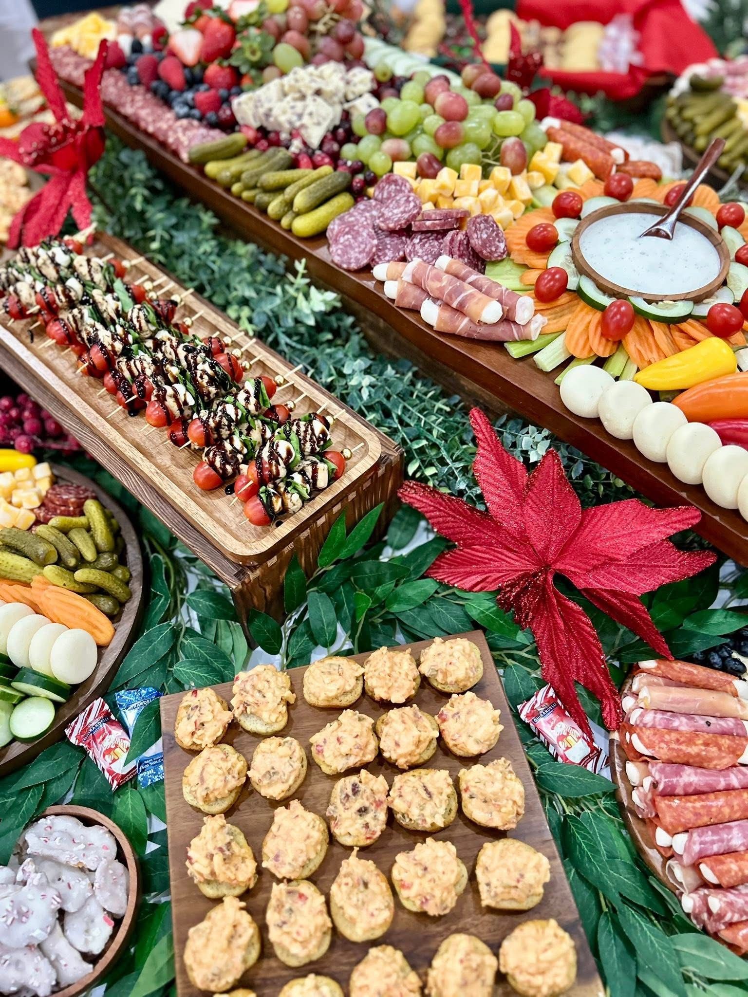 Appetizers on a wooden tray with a large red poinsettia and charcuterie board in the background.