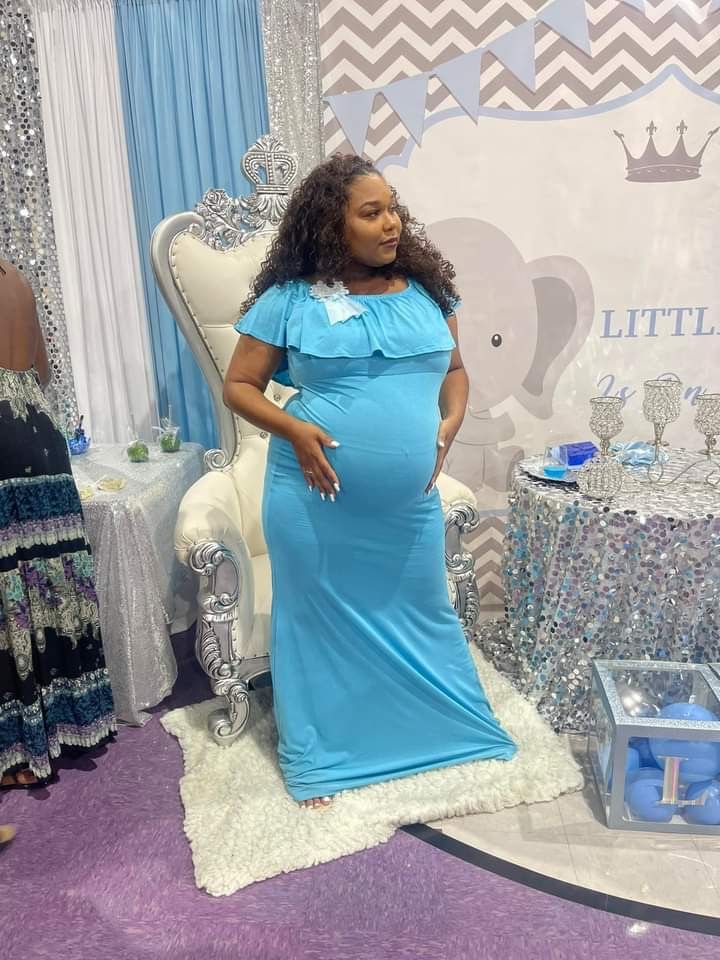 A pregnant woman in a blue dress is standing in front of an elephant backdrop.