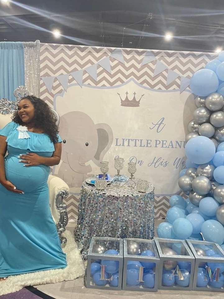 A pregnant woman is standing in front of a wall of balloons at a baby shower.