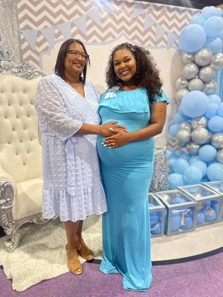 A pregnant woman in a blue dress is standing next to a woman in a white dress at a baby shower.