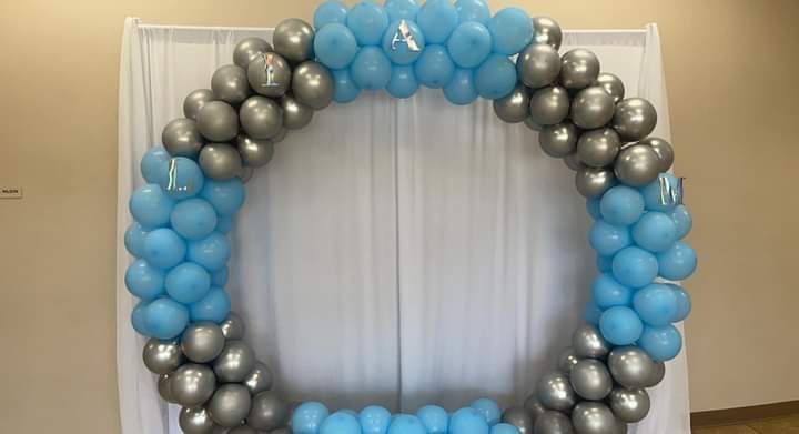 A blue and silver balloon arch is sitting on top of a white curtain.