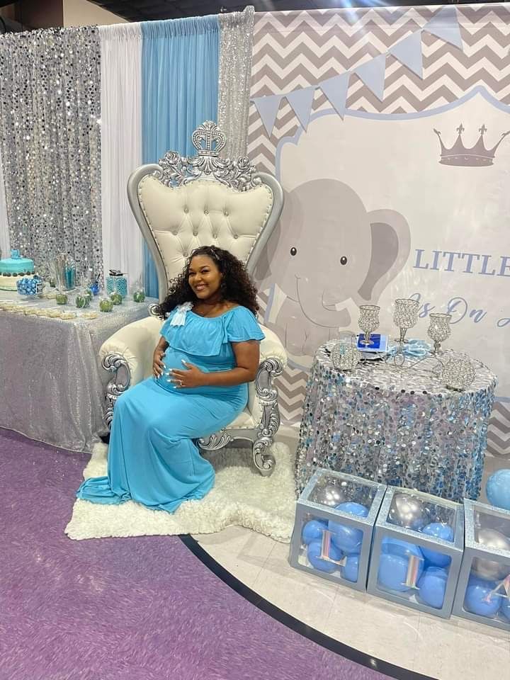 A pregnant woman in a blue dress is sitting in a chair at a baby shower.