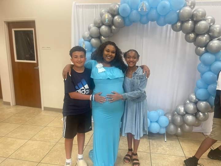 A pregnant woman is posing for a picture with two children at a baby shower.
