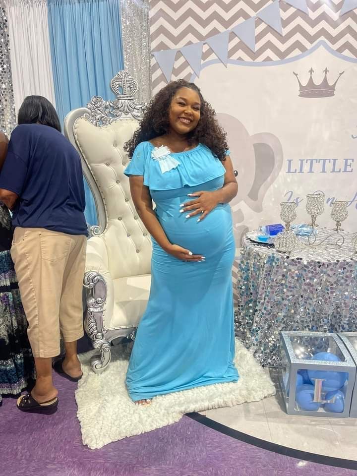 A pregnant woman in a blue dress is standing next to a chair at a baby shower.