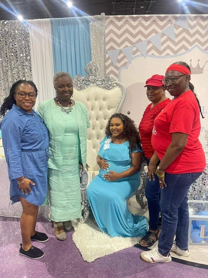 A group of women are posing for a picture with a pregnant woman in a blue dress.