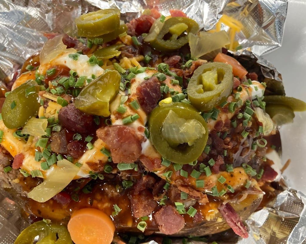 A baked potato topped with cheese , bacon , jalapenos and carrots.