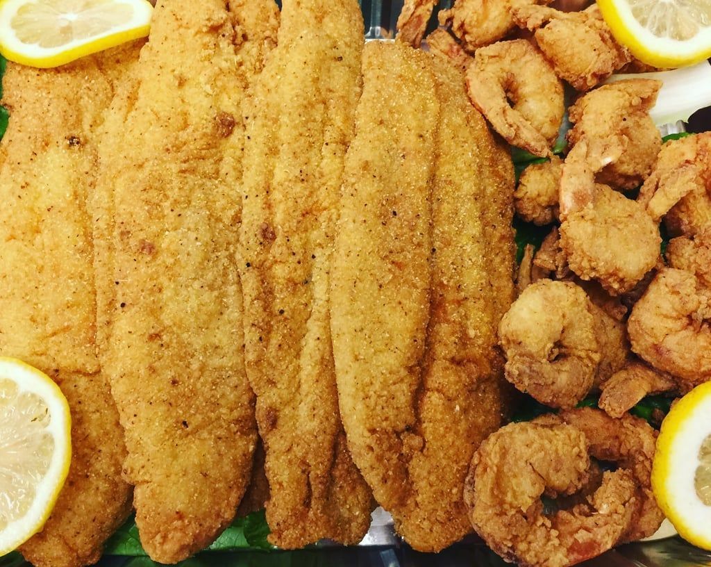 A tray of fried fish and shrimp with lemon wedges.