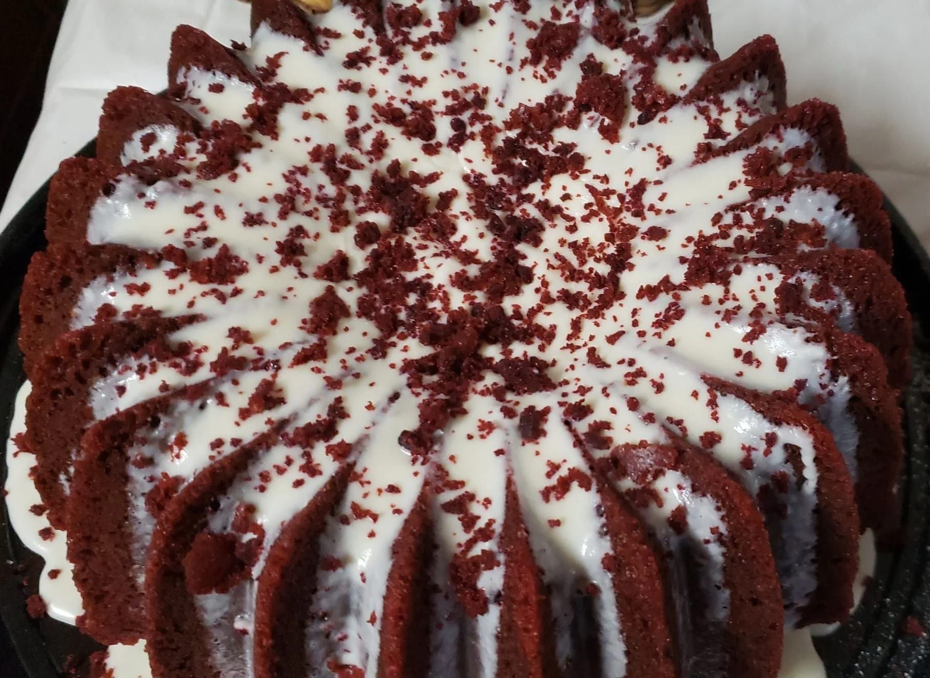 A red velvet bundt cake with white frosting and red sprinkles