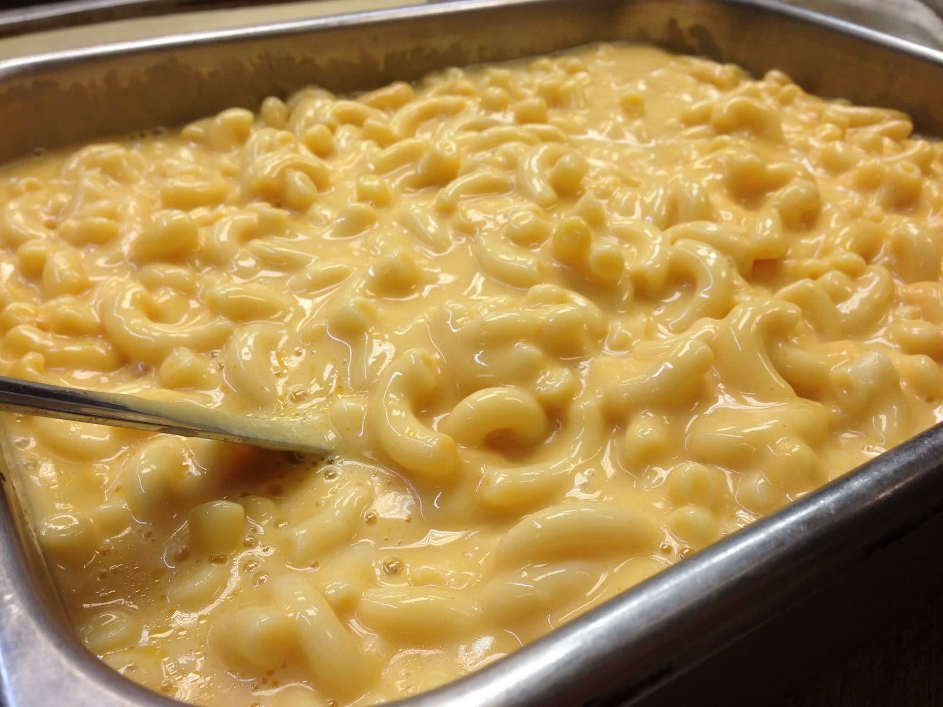 A tray of macaroni and cheese with a spoon in it.