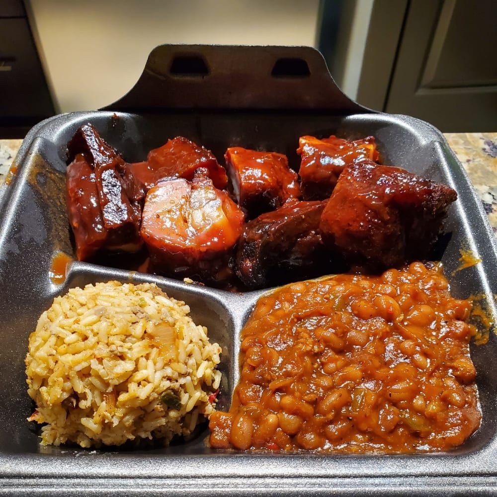 A styrofoam container filled with meat , rice and beans.