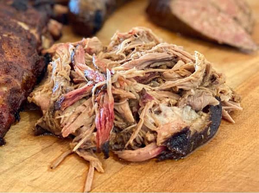 A pile of pulled pork is sitting on a wooden cutting board.