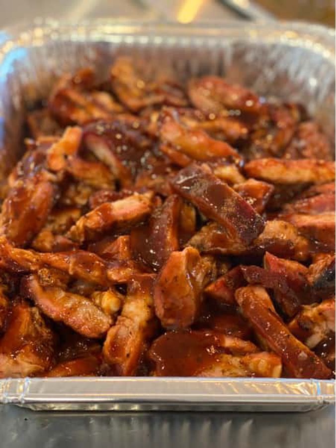 A close up of a tray of meat with barbecue sauce on a table.