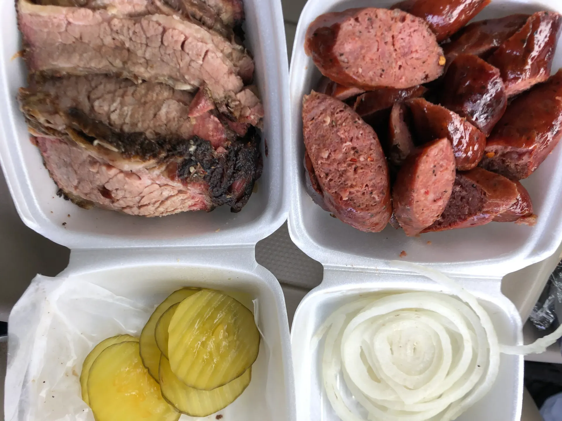 A styrofoam container filled with meat , sausage , pickles and onions.