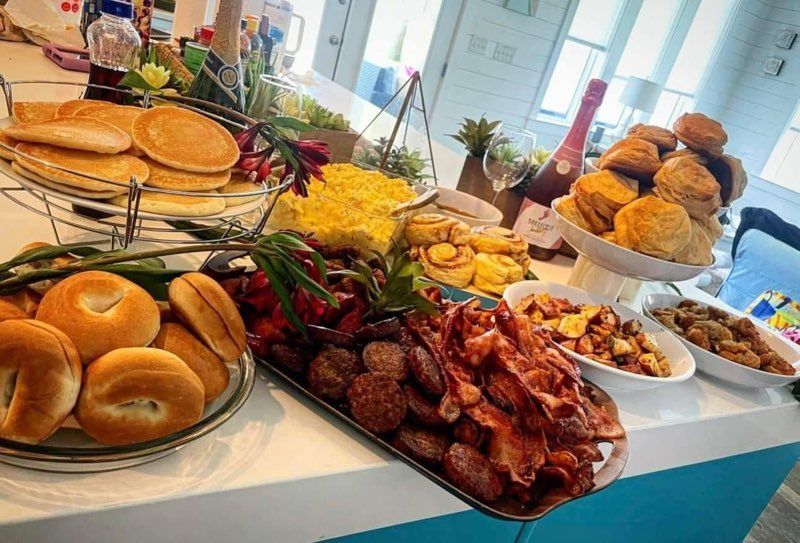A table topped with a variety of food including bacon , pancakes , and scones.