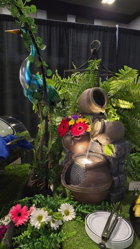 A water fountain is surrounded by flowers and plants on a table.