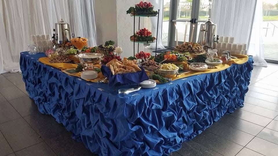 A buffet table with a blue table cloth and a variety of food on it.