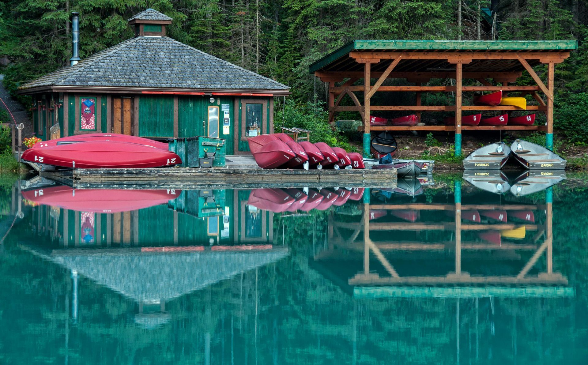 A row of red kayaks are sitting on a dock next to a house.