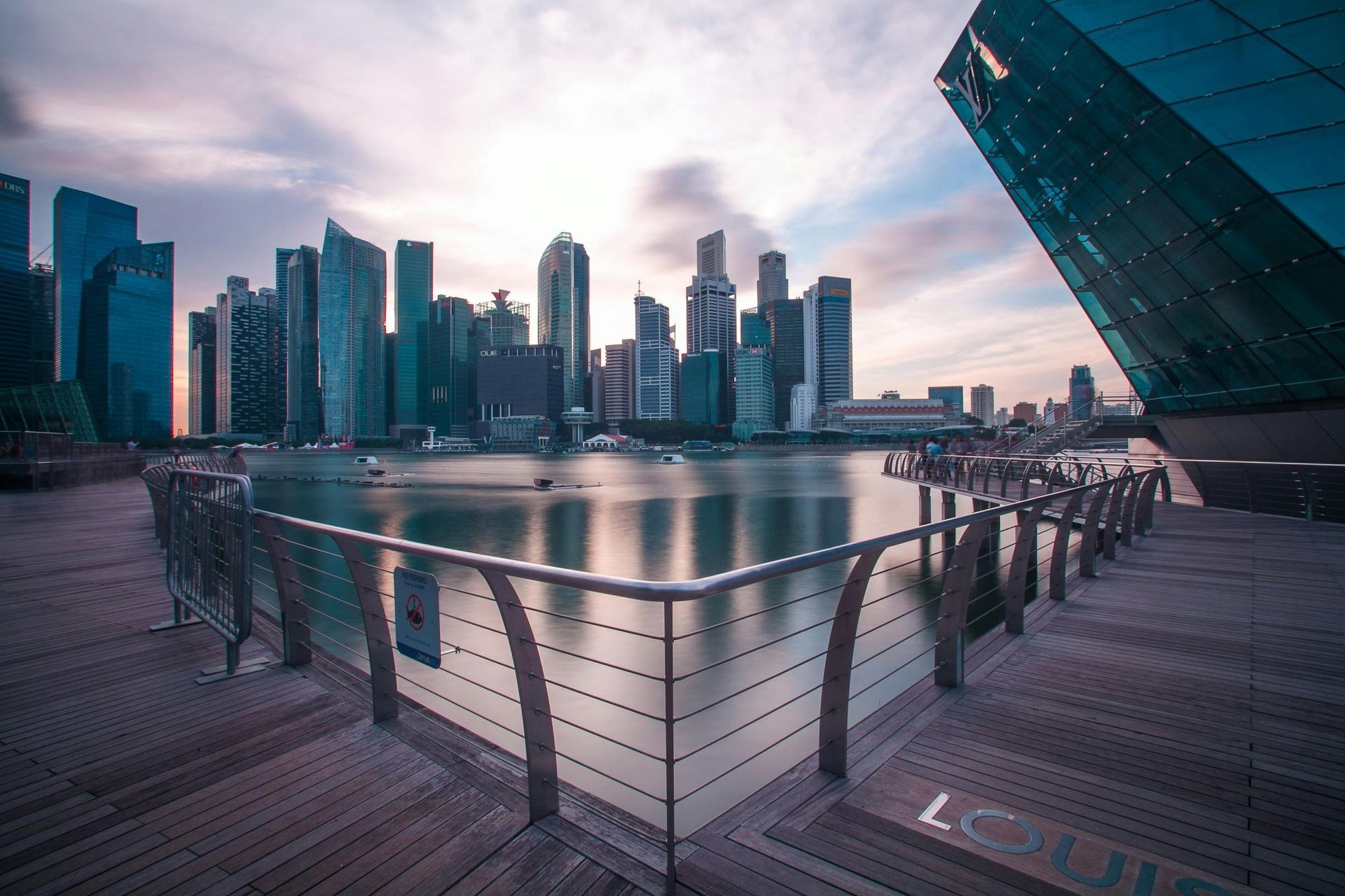 A city skyline with a fence in the foreground and a body of water in the background.