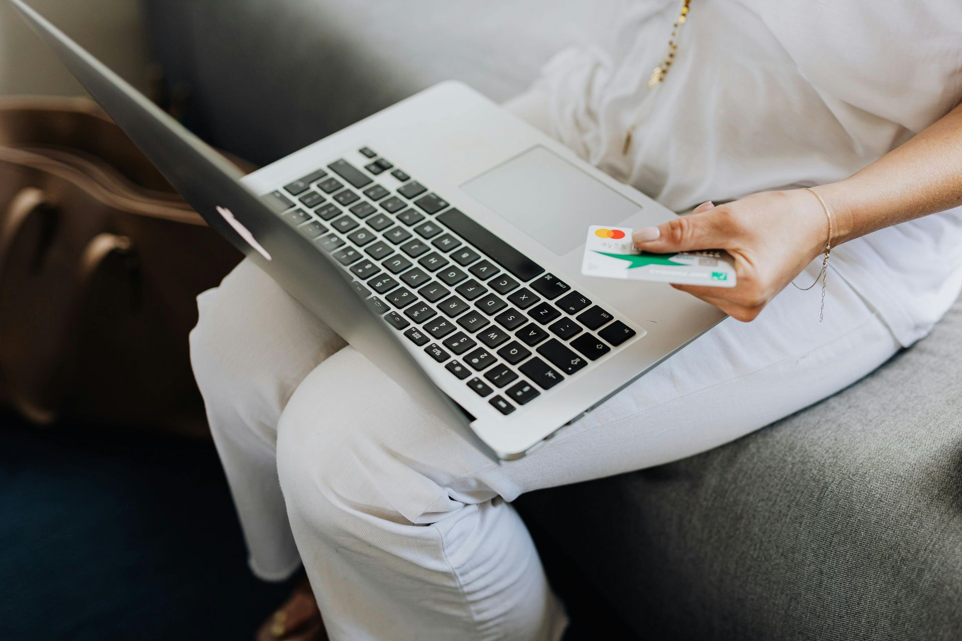 A woman is sitting on a couch using a laptop and holding a credit card.