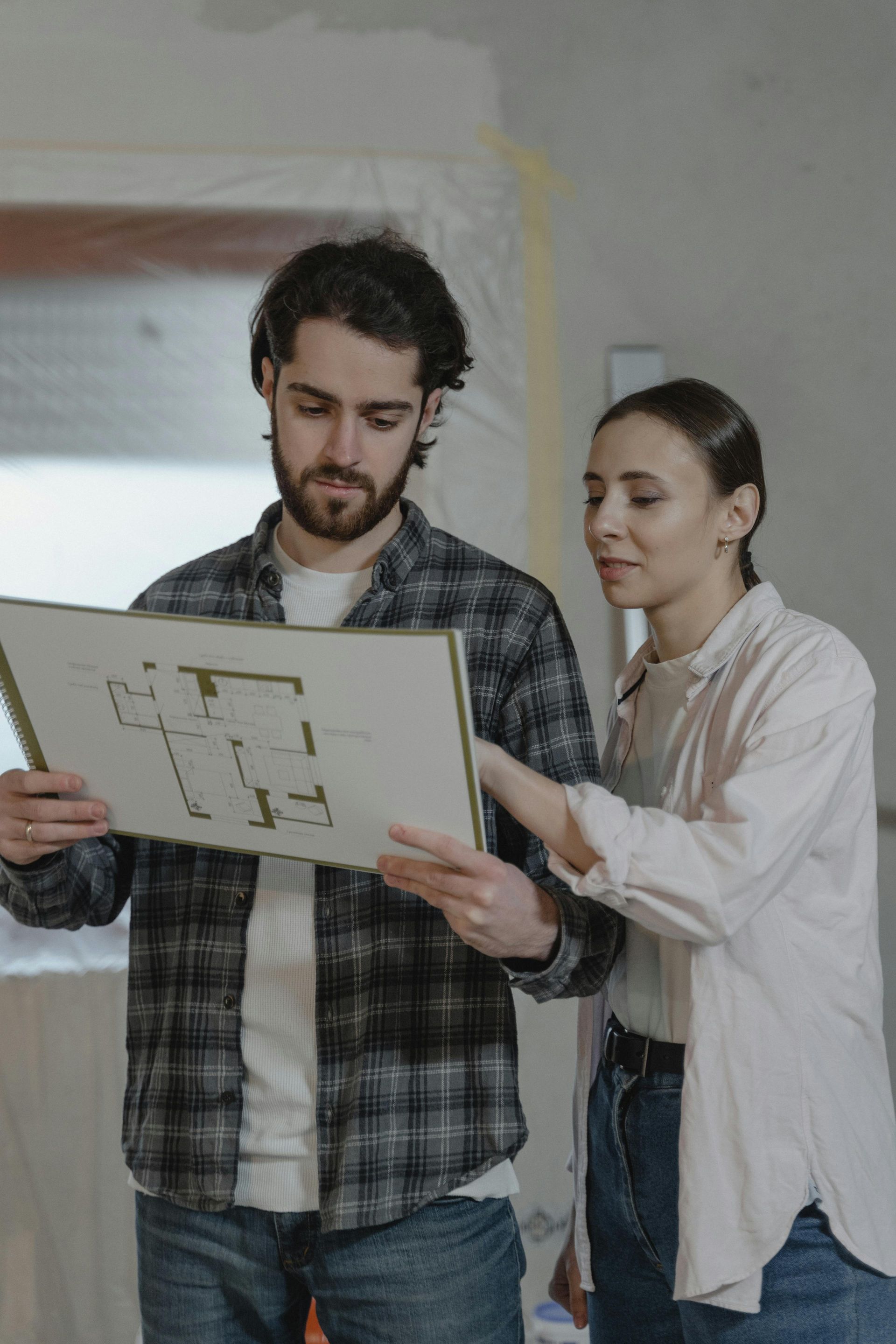 A man and a woman are looking at a floor plan of a house.
