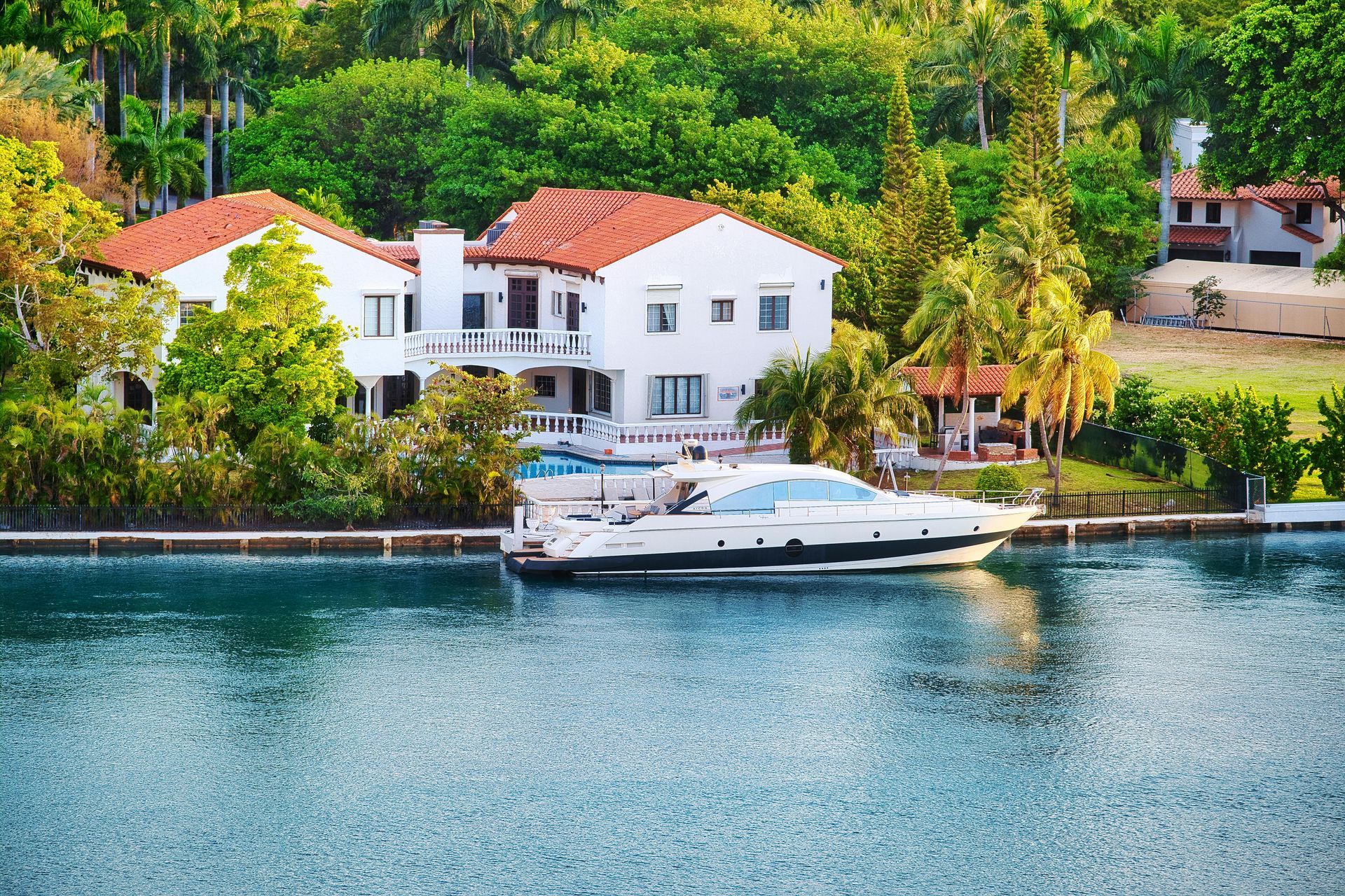 A boat is docked in front of a large house in the water.