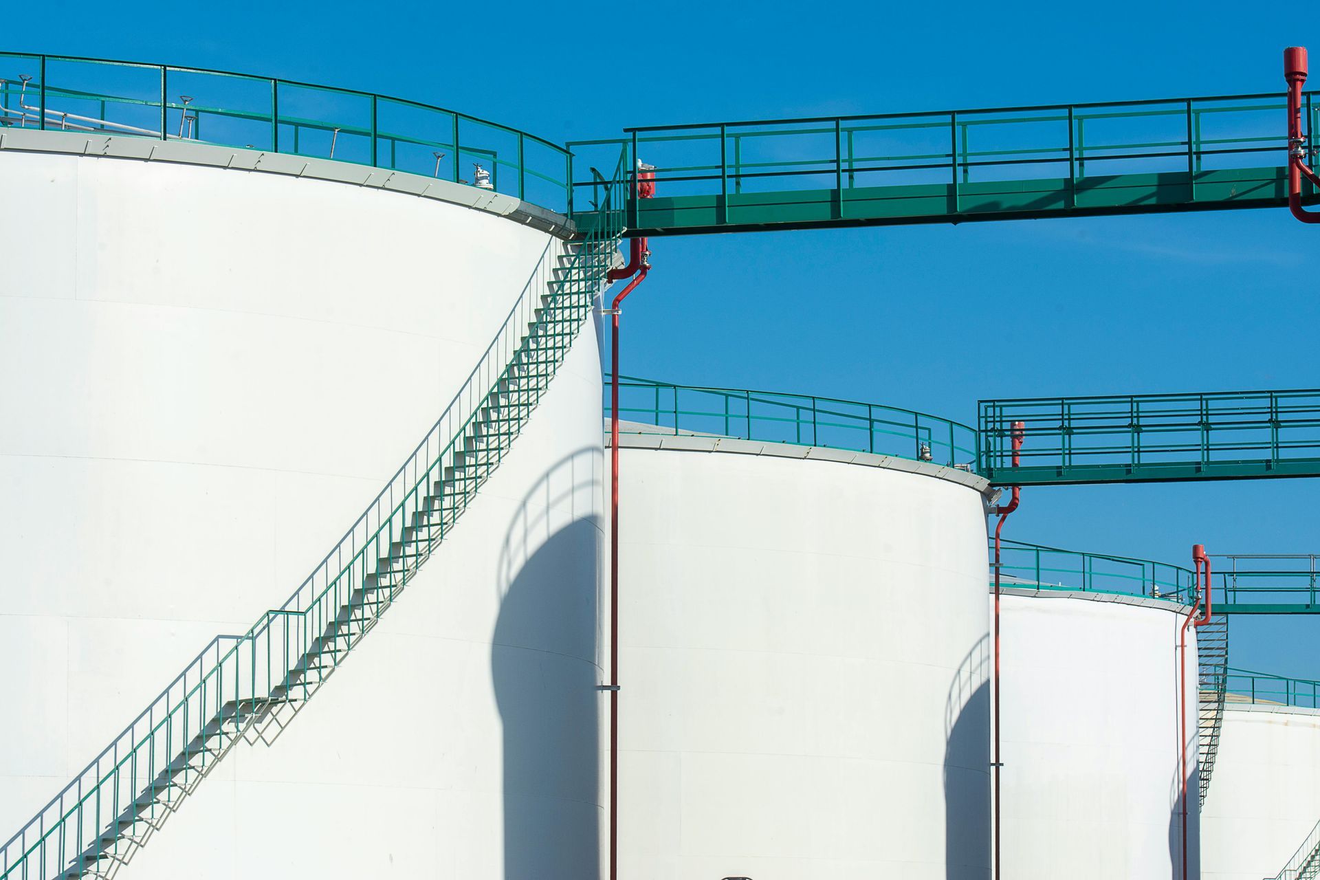 Large white industrial storage tanks with green catwalks against a clear blue sky