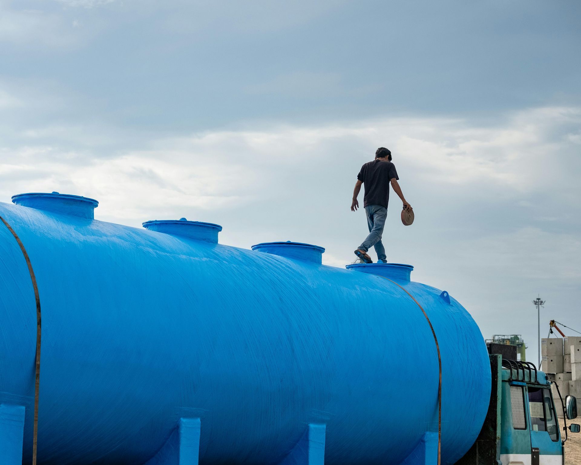 Person walking on top of a large blue storage tank under a cloudy sky