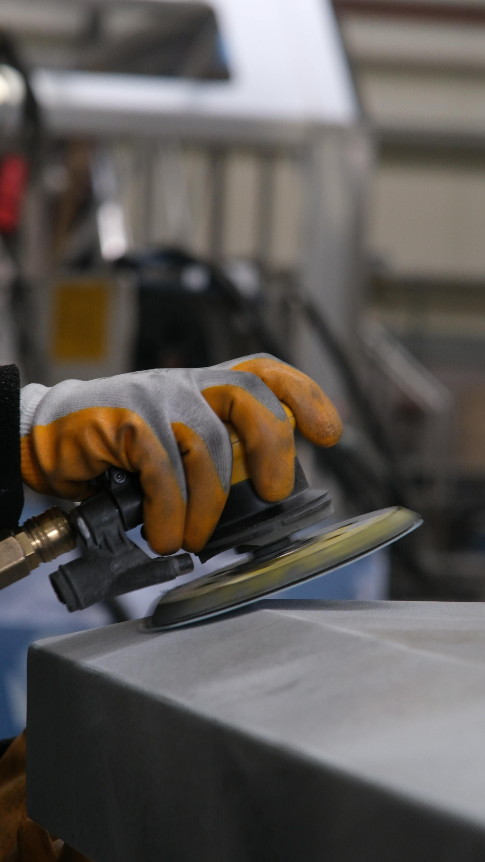 Gloved hand using a power sander on a metal surface in a workshop