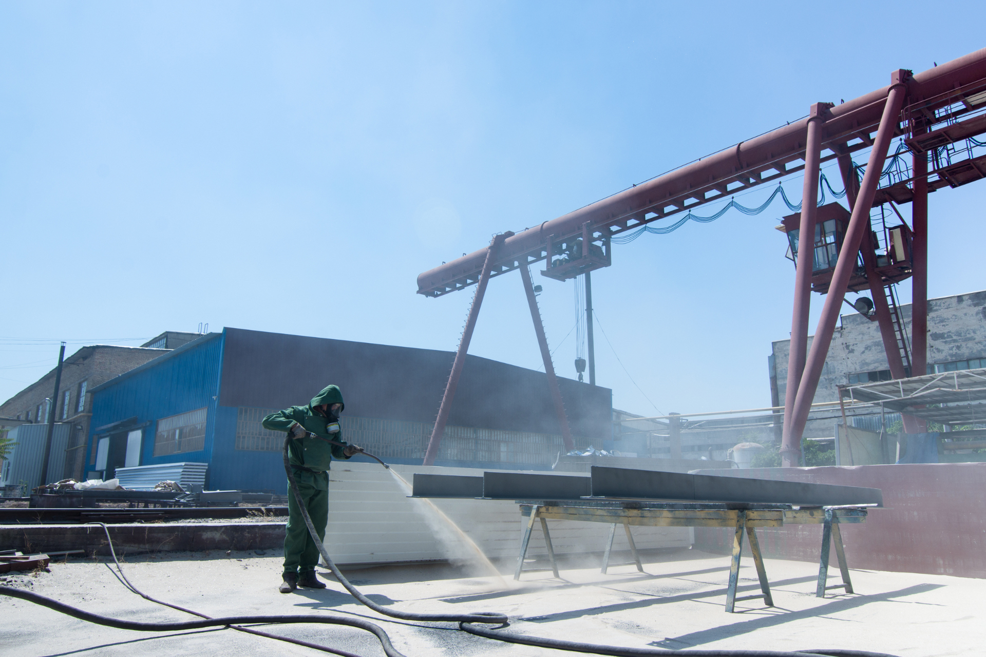 A man in a green suit is sandblasting a piece of metal in a factory.