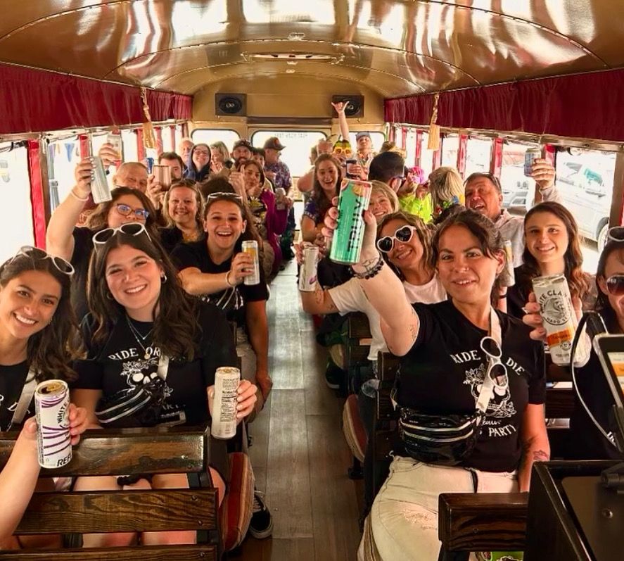 Group of people and a dog posing with a Grinch character in front of a red trolley lit with green lights.