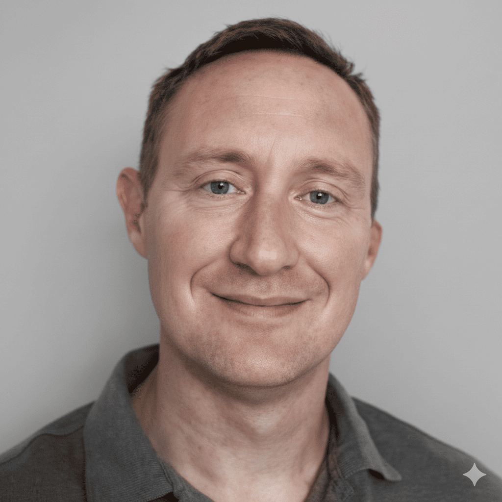 Man with short brown hair, smiling, wearing a gray polo shirt, against a gray background.