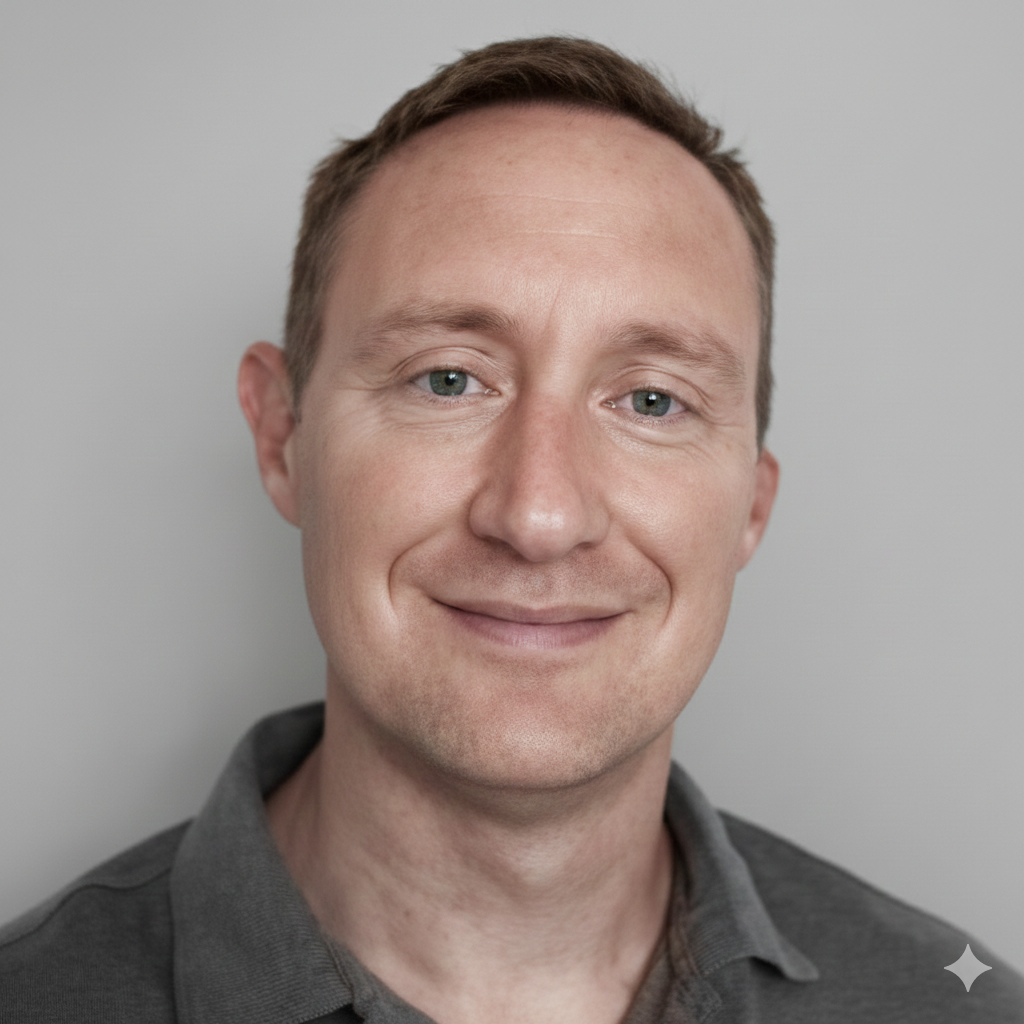 Man with short brown hair, smiling, wearing a gray polo shirt, against a gray background.