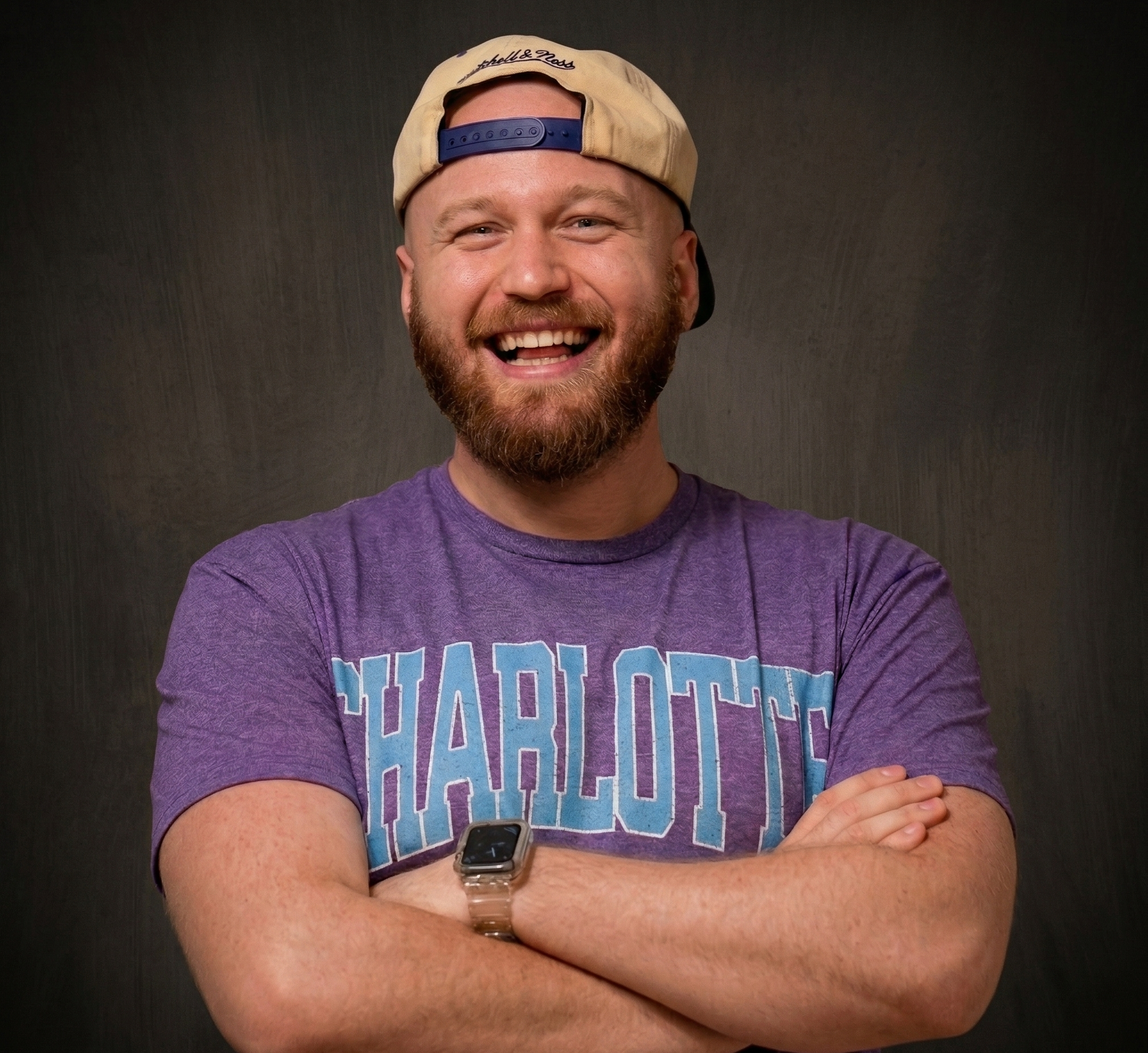 Man with a red beard smiles, yellow parakeet on his shoulder, gray shirt, dark suspenders.
