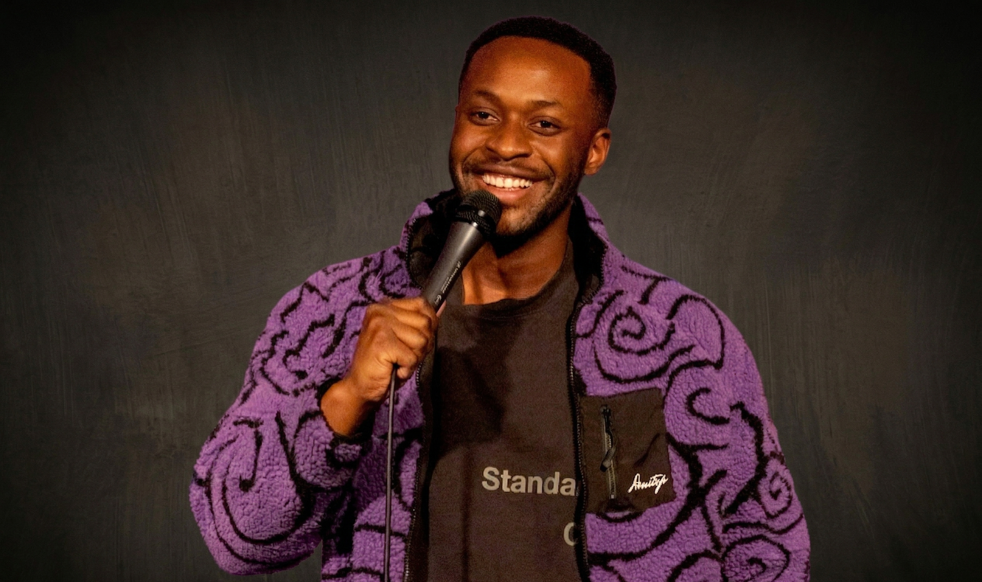 Man with a red beard smiles, yellow parakeet on his shoulder, gray shirt, dark suspenders.