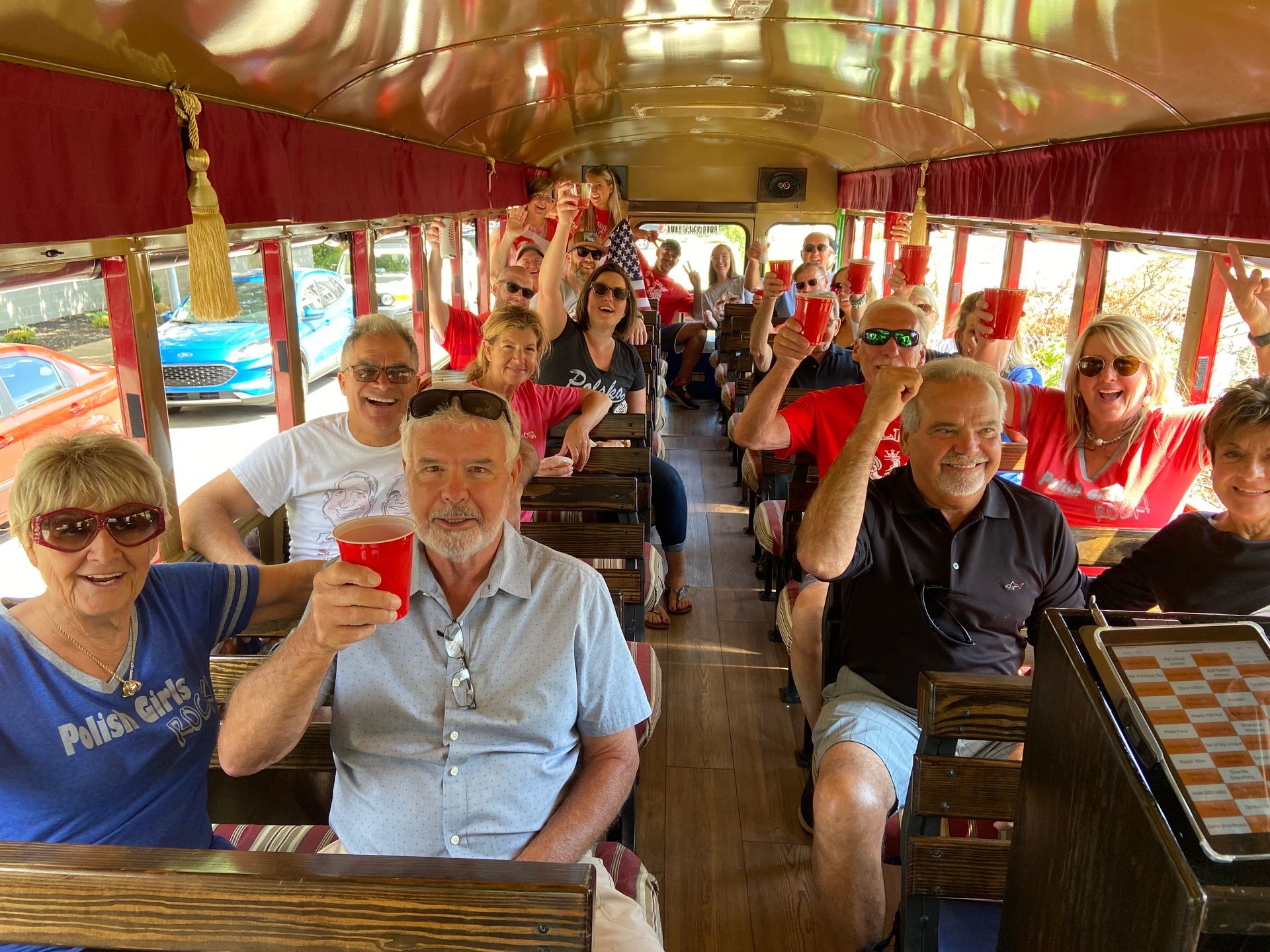 A group of people sitting inside a vintage-style bus, smiling and raising red cups in a toast.
