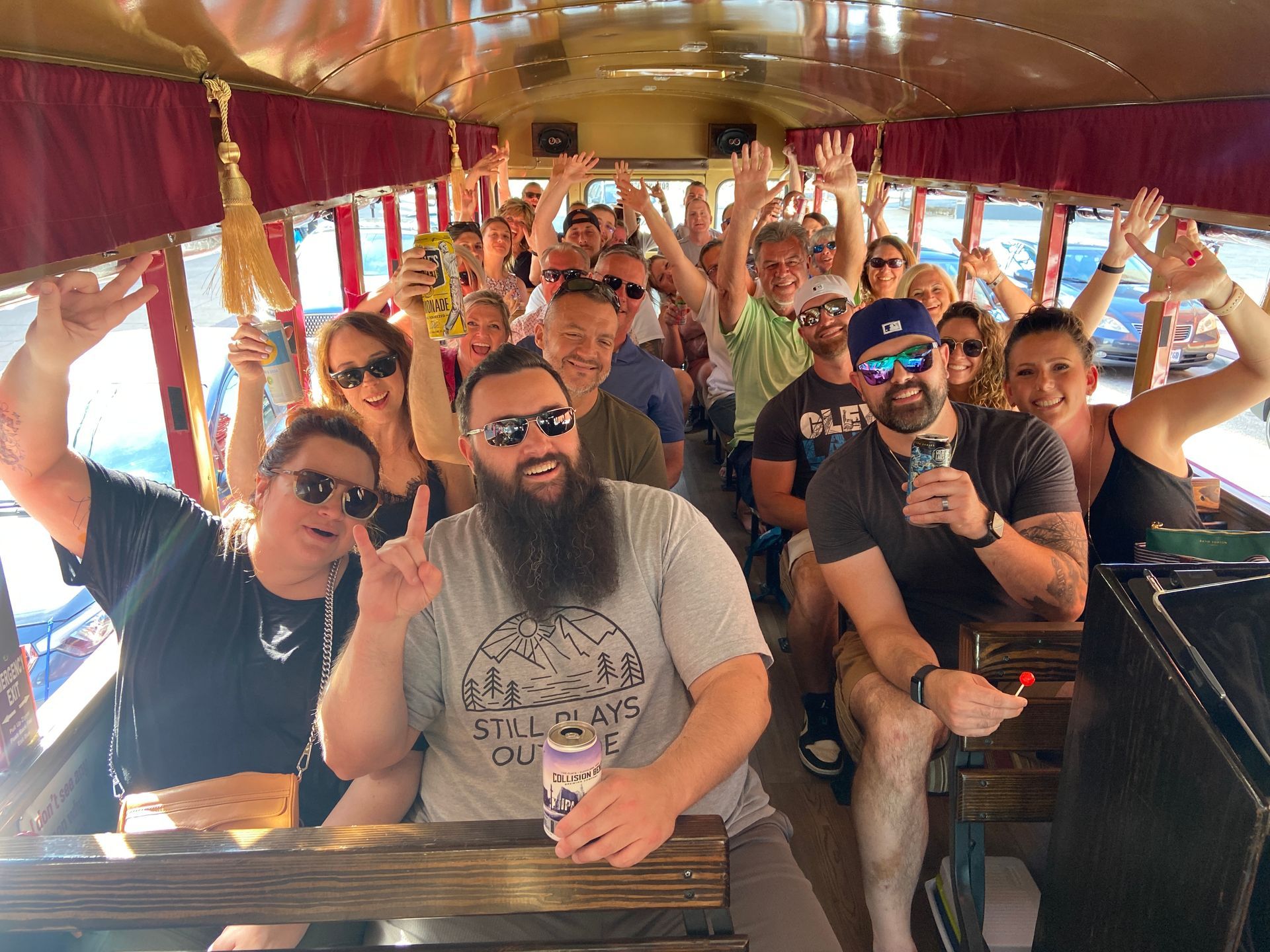 A large group of people celebrating inside a decorated bus, smiling, making hand signs, and holding drinks.