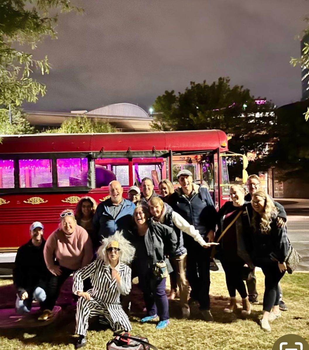 A group of people poses in front of a red bus at night; one person in the foreground wears a striped Beetlejuice costume.