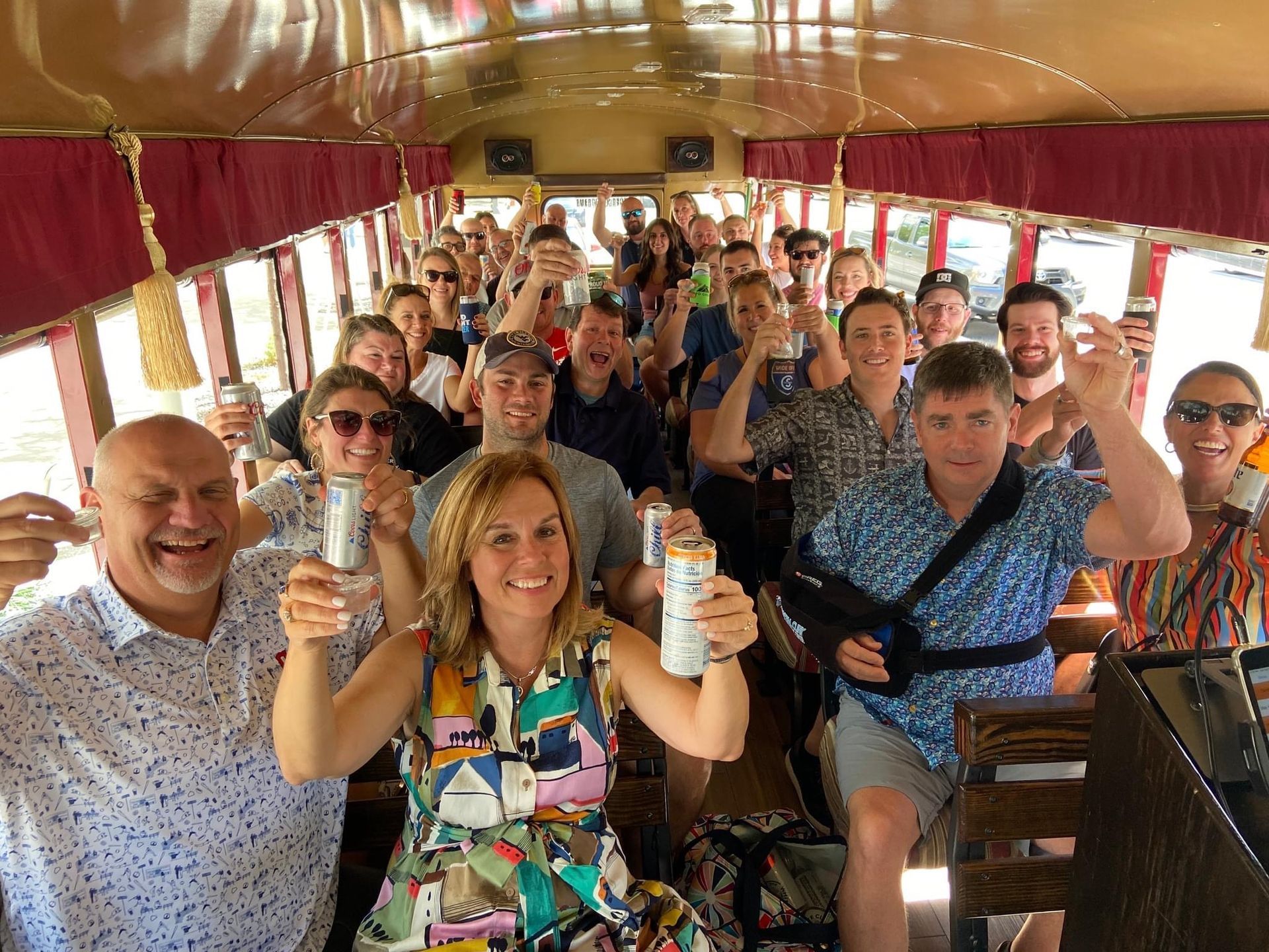 A joyful group inside a decorated trolley car, raising cans for a toast while looking toward the camera.