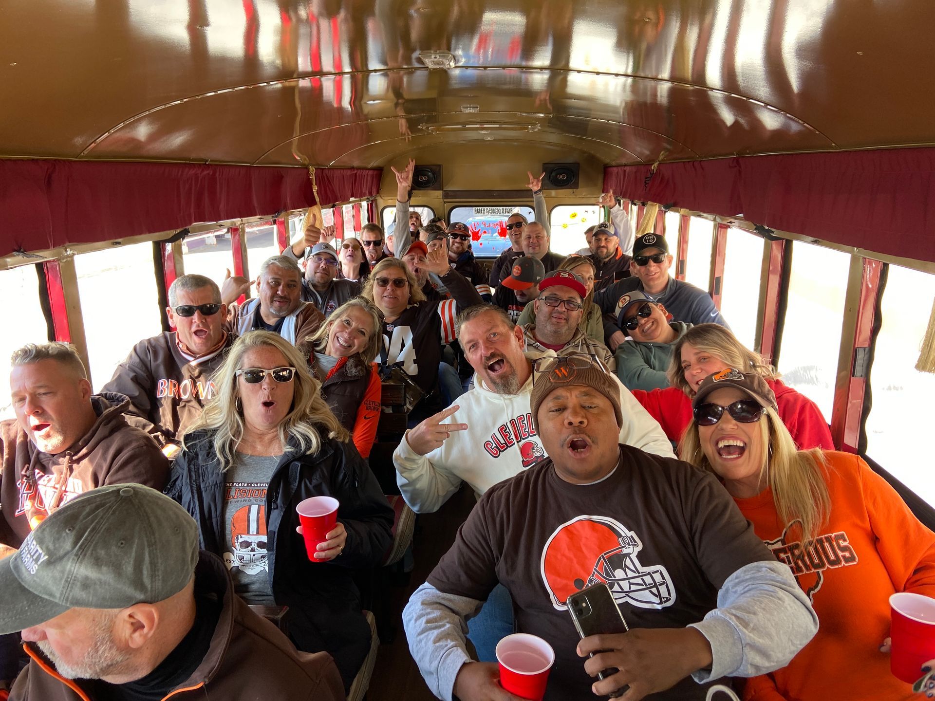 A group of people wearing Cleveland Browns gear celebrating and laughing together inside a bus.
