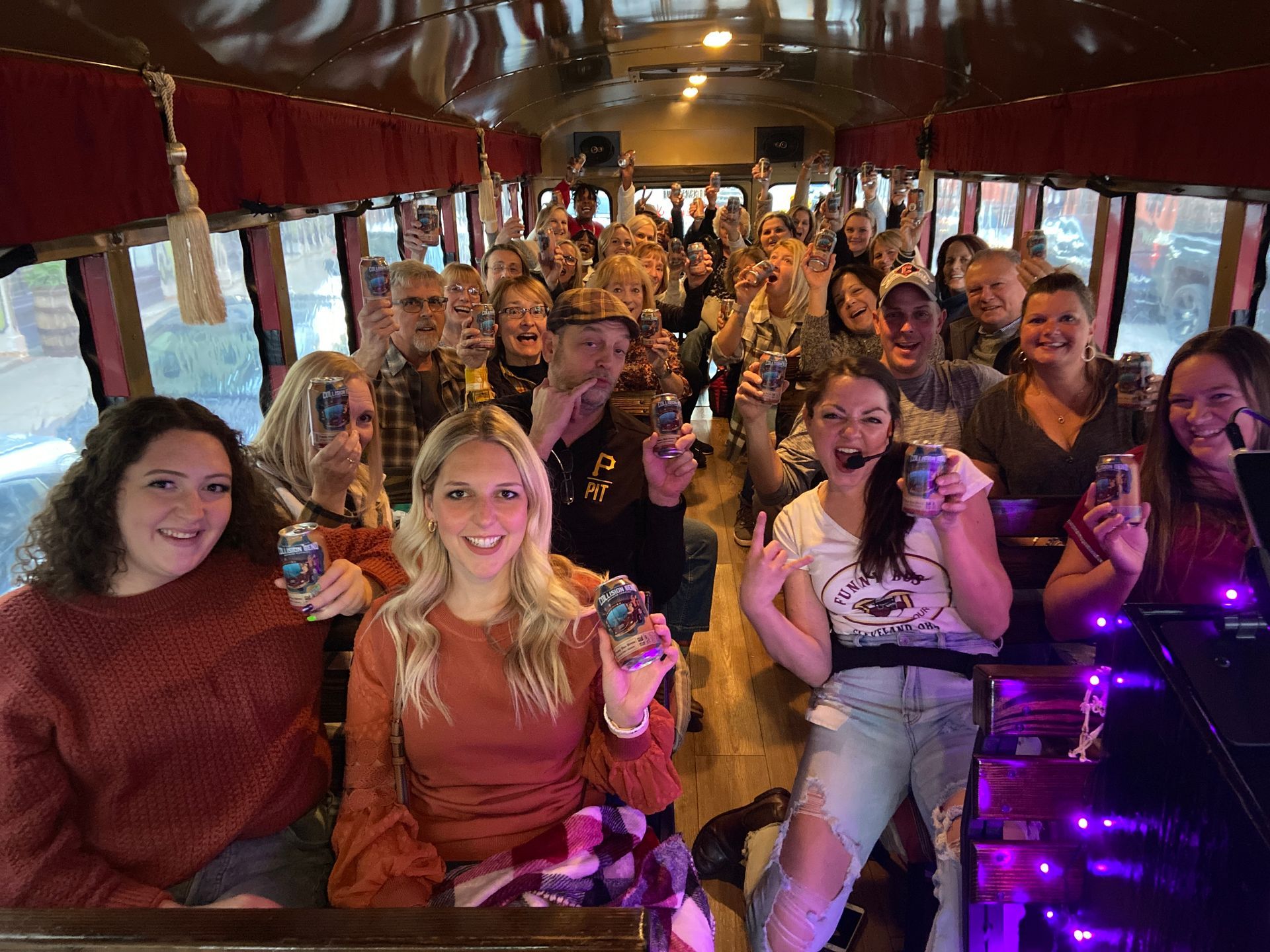 A group of people holding drinks and smiling inside a bus, celebrating together in a lively, social setting.