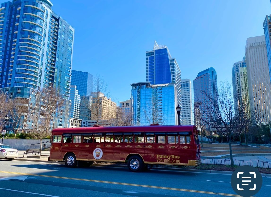 Red city bus on a street with tall blue glass skyscrapers under a clear sky