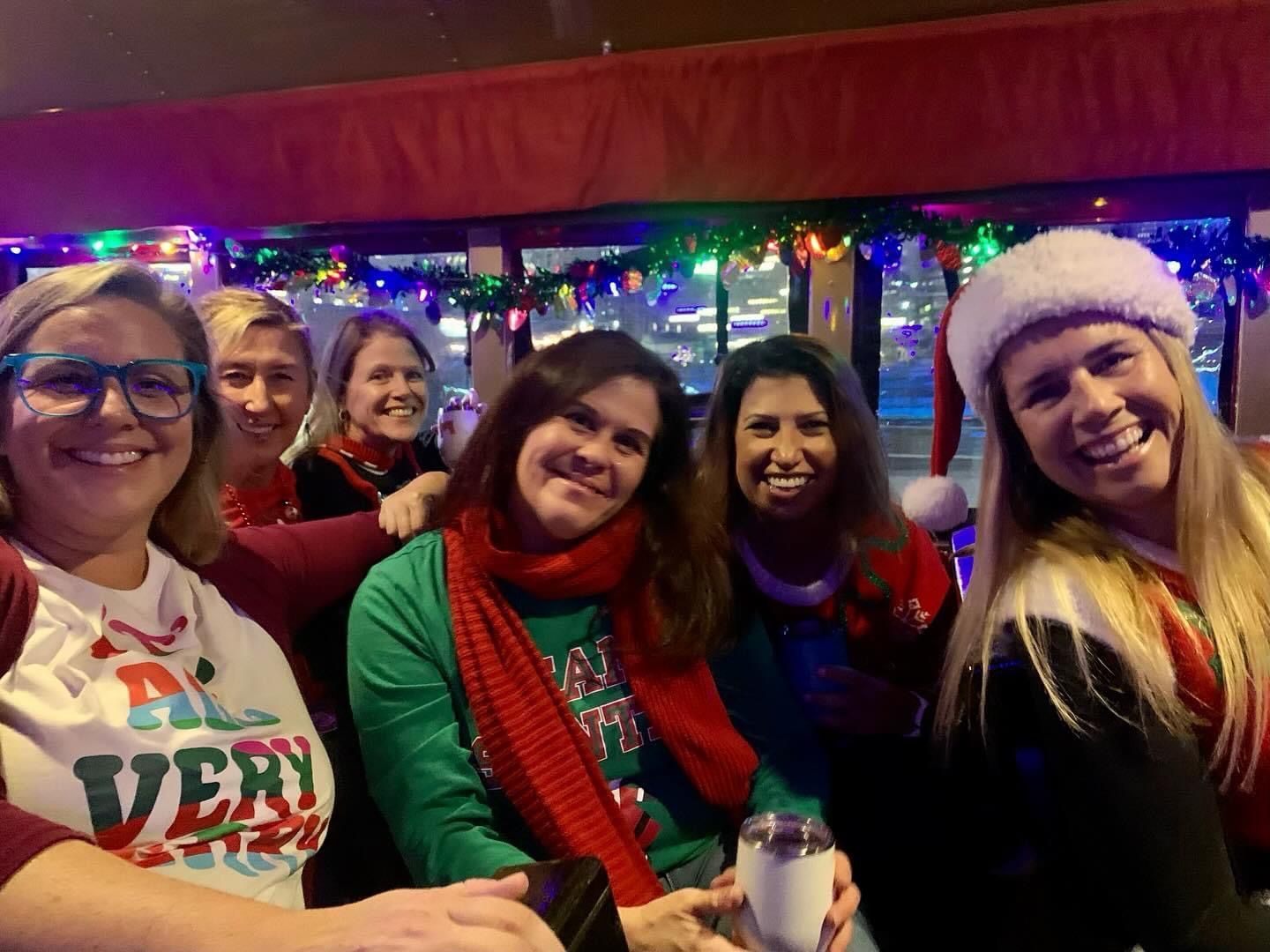 Five friends smiling in festive holiday sweaters and Santa hats at a decorated party.