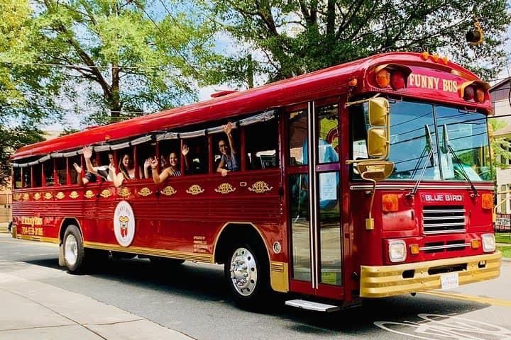 Red open-top tour bus with passengers, driving on a sunny street.