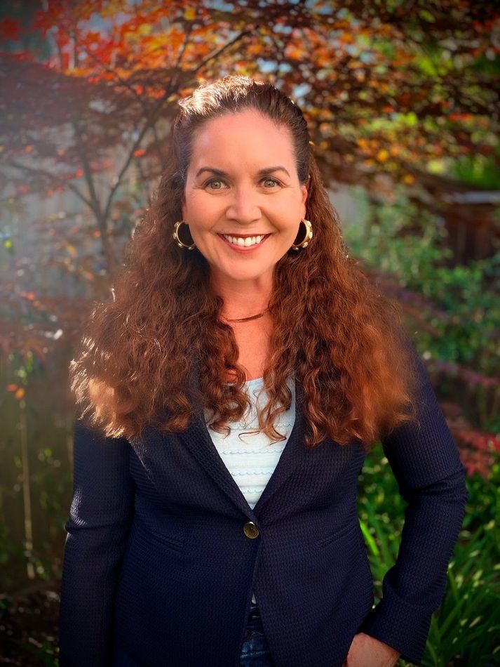 Woman in a navy blazer and white top smiles, posing for a portrait in a studio setting.