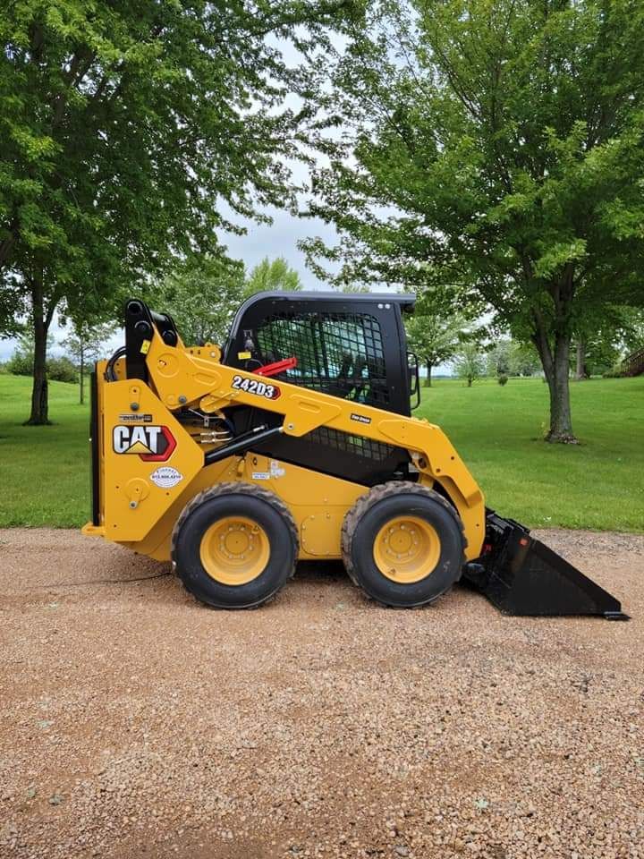 A yellow cat skid steer loader is parked on a gravel road.