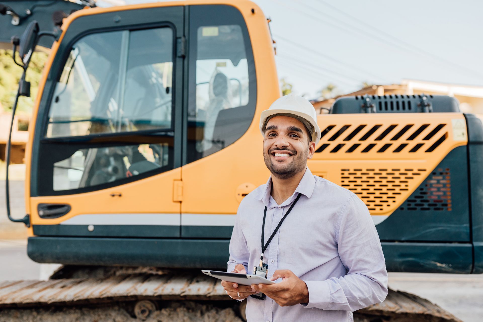 Young engineer at construction site with mini excavator behind him