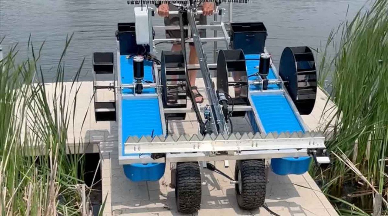 A robot is sitting on a dock next to a body of water.