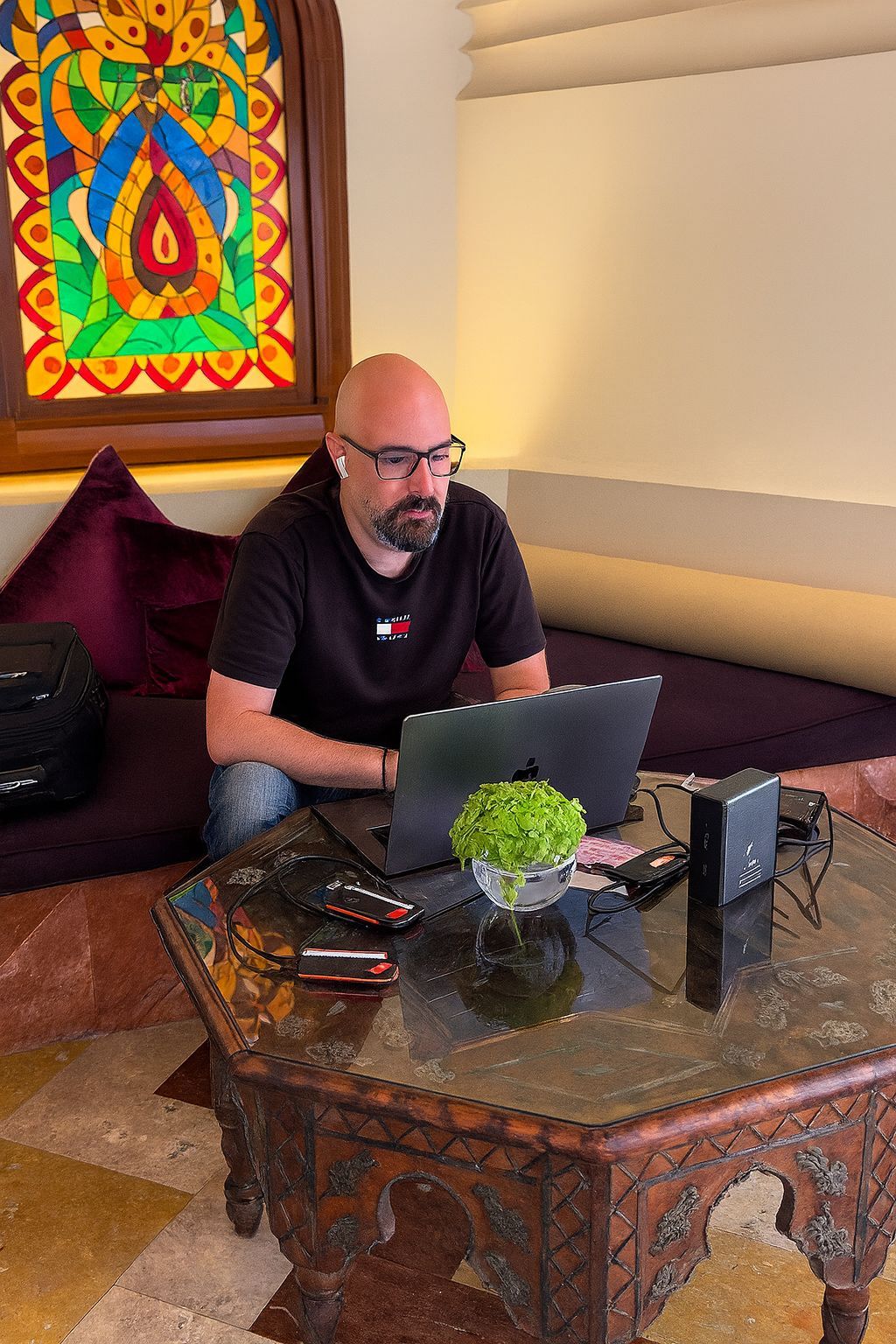 Professional Digital Imaging Technician in Dubai working on a MacBook Pro surrounded by SSD drives and backup equipment inside a luxury Arabic-style setting with stained glass and traditional decor.