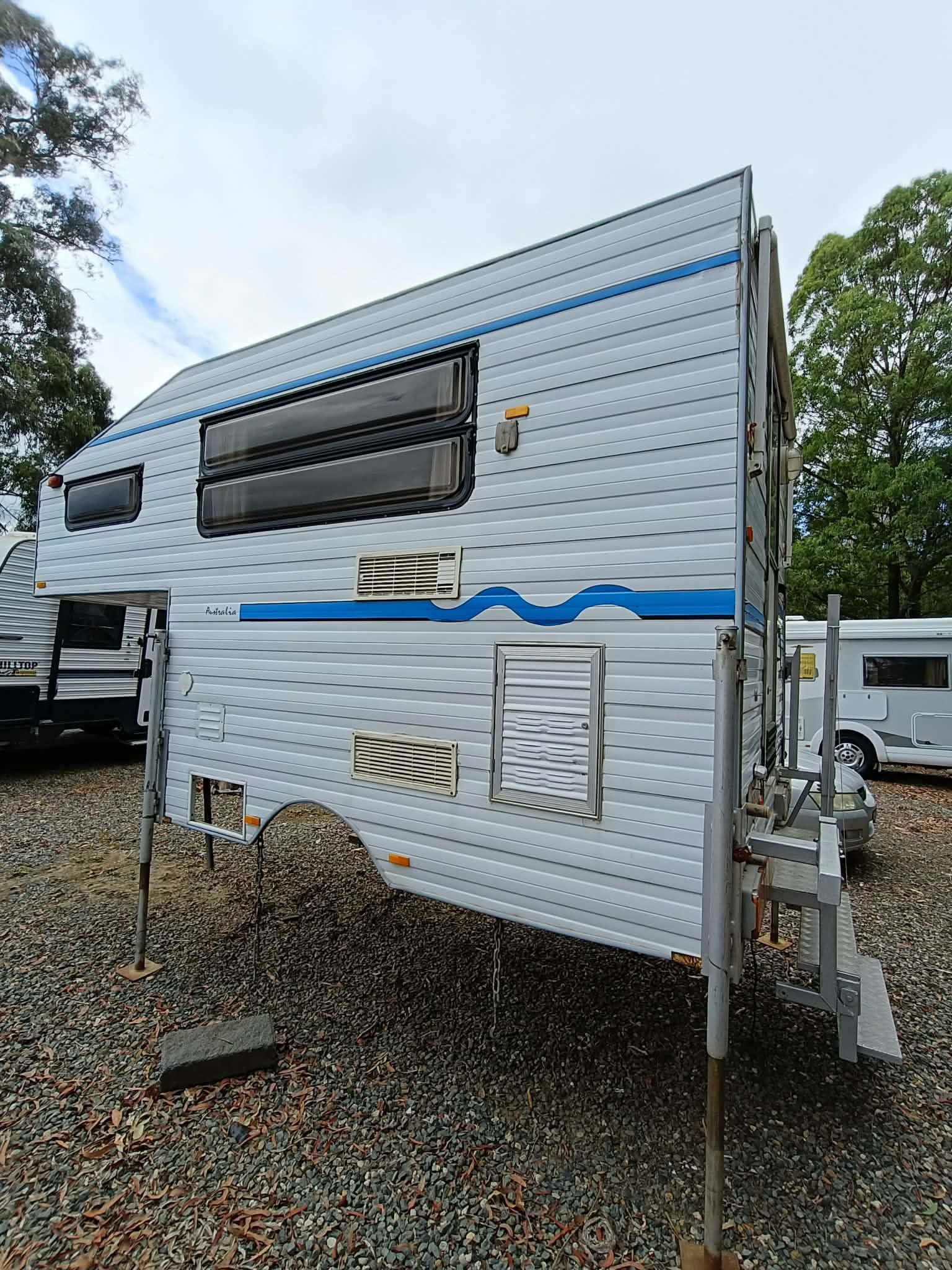 A White and Blue Camper Mounted on Posts, Parked Outdoors — Great Lakes Caravans & RV P/L In Nabiac, NSW